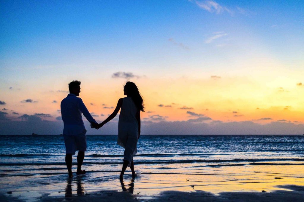 man and woman holding hands walking on seashore during 1024960